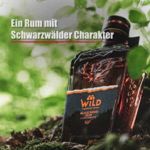 Eine Flasche Black Wood Rum steht auf moosbewachsenem Boden in einem Wald, darüber die Aufschrift "Ein Rum mit Schwarzwälder Charakter".
