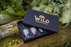 Die Wild Tasting-Box Edelbrände & Geiste, eine schwarze Geschenkbox mit drei kleinen Flaschen, steht auf moosbewachsenem Holz im Freien.