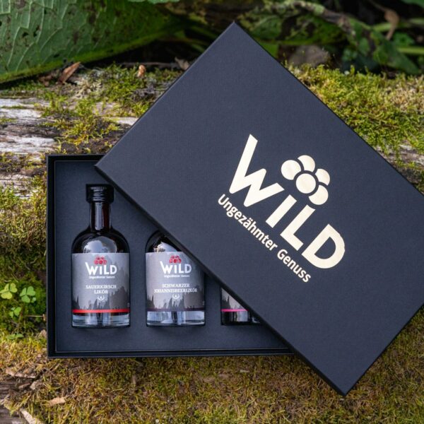 Die Wild Tasting-Box Liköre ist eine schwarze Geschenkbox mit drei kleinen Likörflaschen, die mit der Aufschrift "WILD Ungezähmter Genuss" versehen sind und im Freien auf Moos stehen.