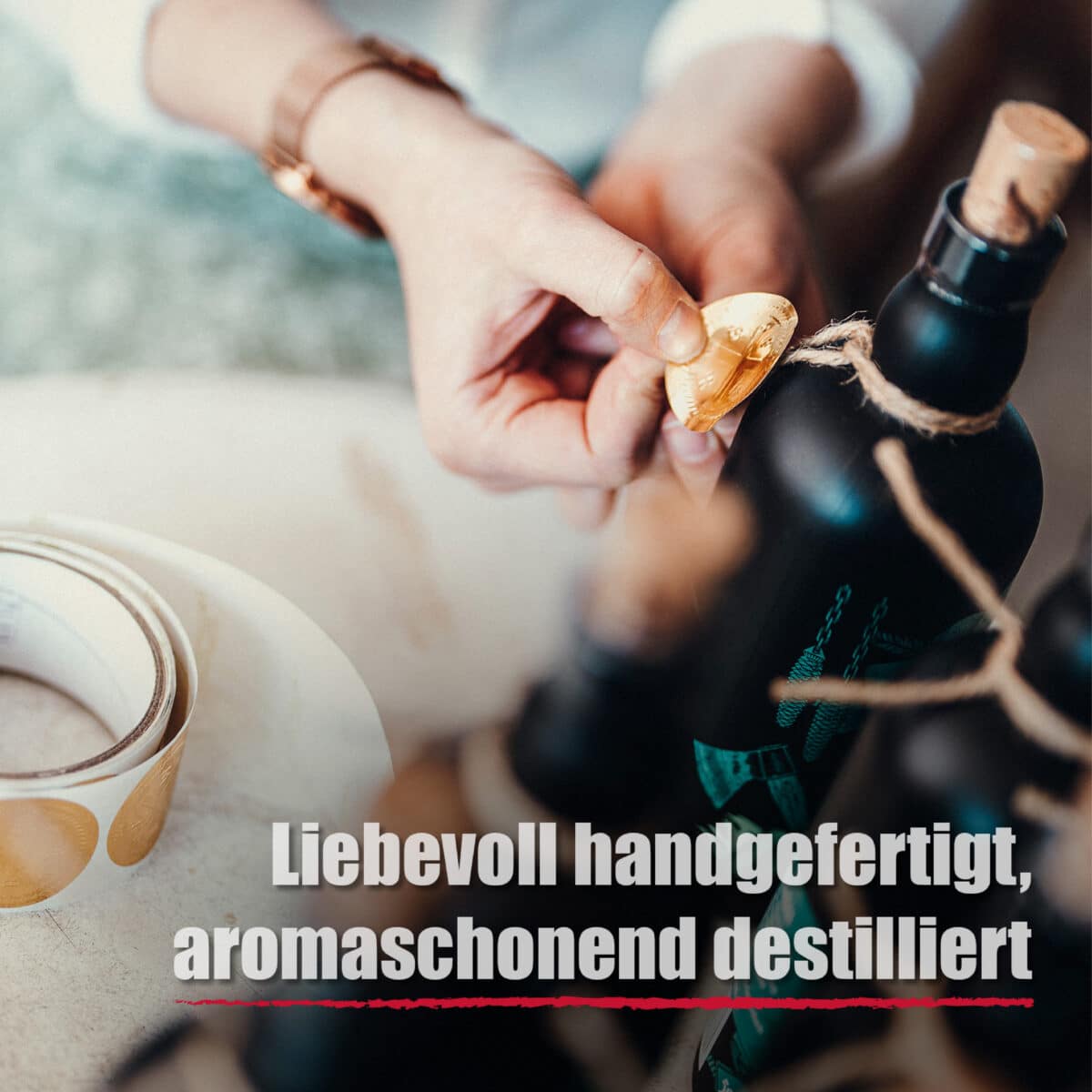 Eine Person klebt ein rundes goldenes Etikett auf eine Flasche Blackforest Wild Gin Creative; der deutsche Text lautet Liebevoll handgefertigt, aromaschonend destilliert.