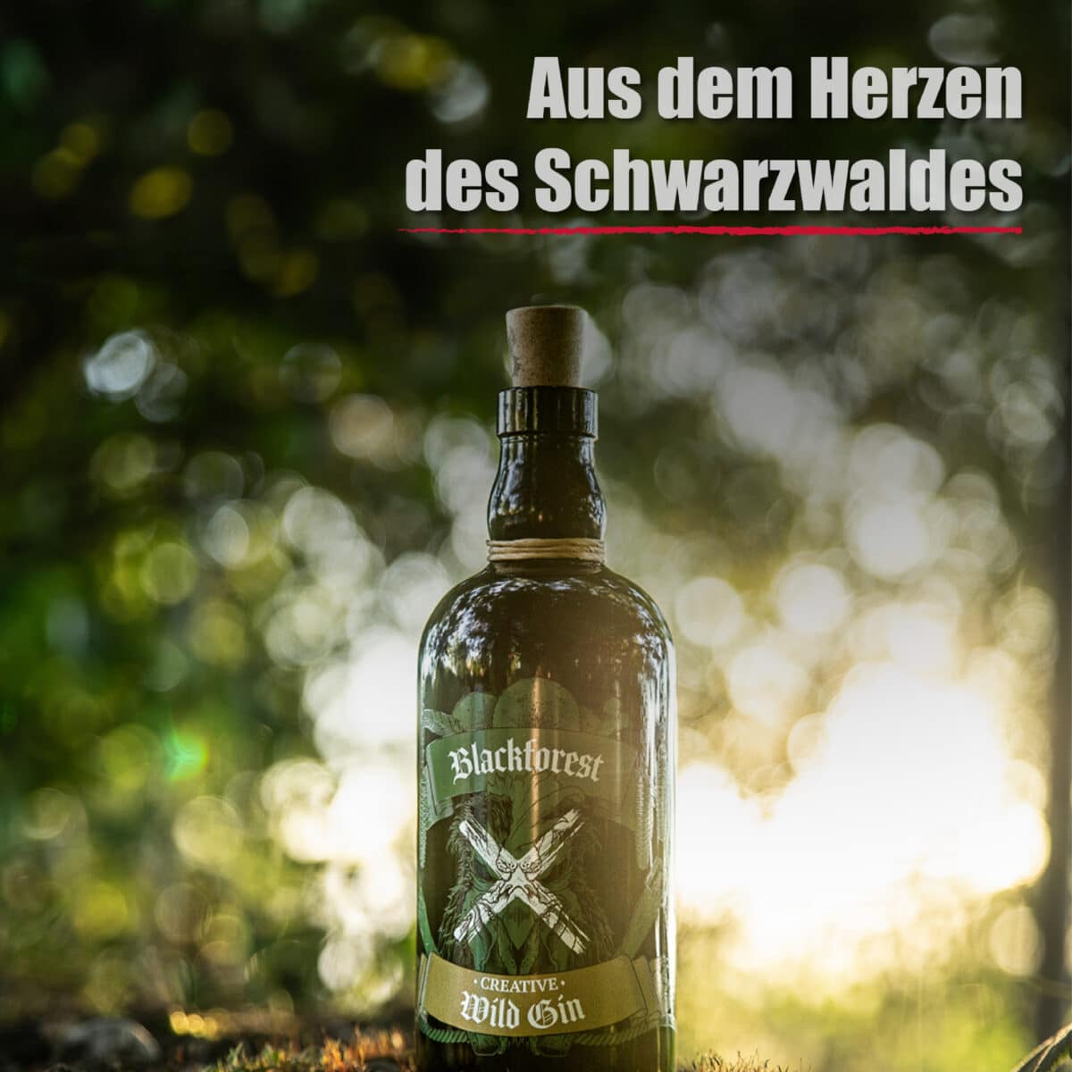 Eine Flasche Blackforest Wild Gin Creative steht im Freien mit verschwommenen Bäumen und Sonnenlicht im Hintergrund. Der Text darüber lautet: "Aus dem Herzen des Schwarzwaldes".