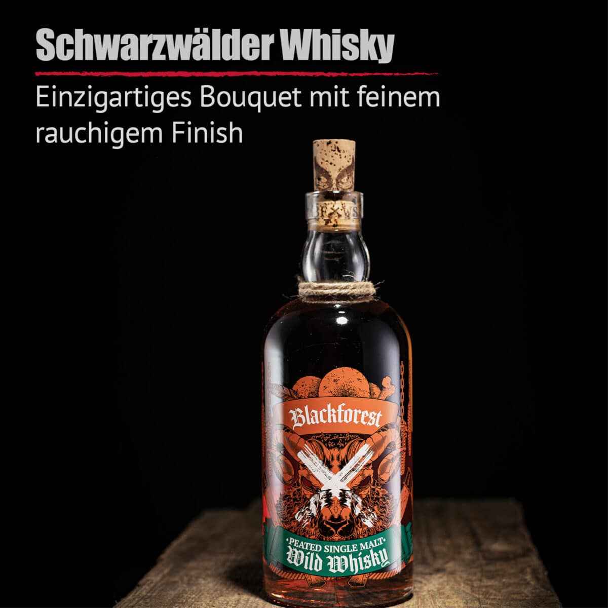 Eine Flasche Blackforest Wild Whisky Peated Single Malt mit einem dekorativen Etikett, einem Korkverschluss und einer Schnur um den Hals steht vor einem schwarzen Hintergrund, über dem ein deutscher Text steht.