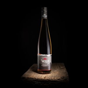 Eine Flasche Wild Apfelwein Grand Cru ruht auf einer hölzernen Oberfläche vor einem schwarzen Hintergrund.