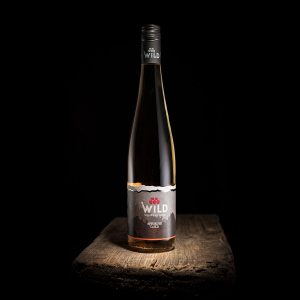 Eine Flasche Wilder Wein mit einem dunklen Etikett steht auf einer rustikalen Holzfläche vor einem schwarzen Hintergrund.