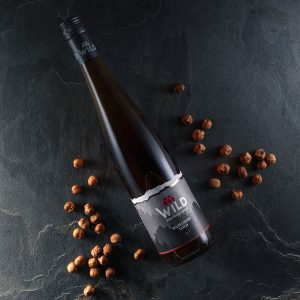 Eine Flasche Wild-Likör liegt auf einer dunklen Steinfläche, umgeben von verstreuten Haselnüssen.