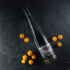 Eine Flasche Wein der Marke Wild liegt auf einer dunklen Steinfläche, umgeben von kleinen gelben Früchten.