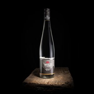 Eine Klarglasflasche mit Mineralwasser der Marke Wild steht auf einer rustikalen Holzfläche vor einem schwarzen Hintergrund.