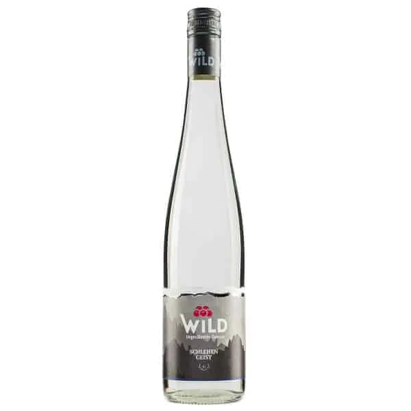 Eine Klarglasflasche des Obstbrandes der Marke Wild mit der Aufschrift "Schlehen Geist", mit einem silbernen Verschluss und einem grauen Etikett mit Berggrafik.