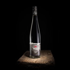 Eine klare Glasflasche mit Wild Squid Gin steht auf einer rustikalen Holzoberfläche vor einem schwarzen Hintergrund.