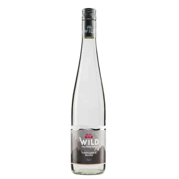 Eine Klarglasflasche der Spirituose Topinambur der Marke Wild mit einem silbernen Verschluss und einem Etikett mit Bergmotiven.