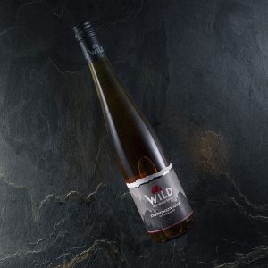 Eine Flasche Wilder Wein mit einem dunklen Etikett liegt schräg auf einer strukturierten schwarzen Steinfläche.