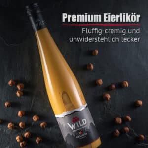 Eine Flasche Eierlikör Haselnuss ruht auf einer dunklen Steinfläche, umgeben von Haselnüssen, und ein deutscher Text hebt die cremige, flauschige Textur und den unwiderstehlich köstlichen Geschmack hervor.
