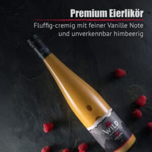 Eine Flasche Eierlikör Himbeere auf einer dunklen Oberfläche, auf der ein deutscher Text über den cremigen Vanille- und Himbeergeschmack steht.