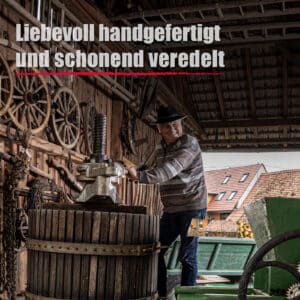 Ein Mann bedient eine traditionelle hölzerne Weinpresse in einer rustikalen Scheune mit alten Wagenrädern; der deutsche Text lautet: Liebevoll handgefertigt und sanft veredelt Schwarzer Johannisbeerlikör.