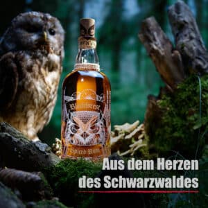 Eine Flasche Blackforest Wild Spiced Rum Barrique ruht auf Moos in einem Wald mit einer Eule in der Nähe; der Text lautet "Aus dem Herzen des Schwarzwaldes".