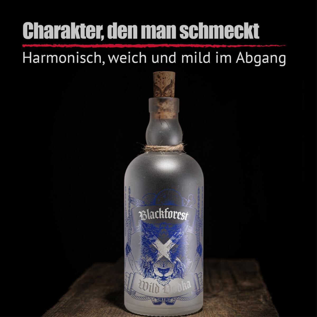 Eine Milchglasflasche von Blackforest Wild Vodka mit blauem Design, Korkverschluss und Seildetail wird auf einer Holzfläche mit dunklem Hintergrund ausgestellt. Der deutsche Text darüber stellt Blackforest Wild Vodka vor.