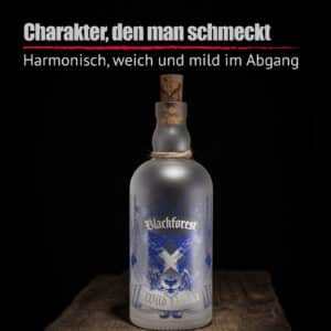 Eine Milchglasflasche von Blackforest Wild Vodka mit blauem Design, Korkverschluss und Seildetail wird auf einer Holzfläche mit dunklem Hintergrund ausgestellt. Der deutsche Text darüber stellt Blackforest Wild Vodka vor.