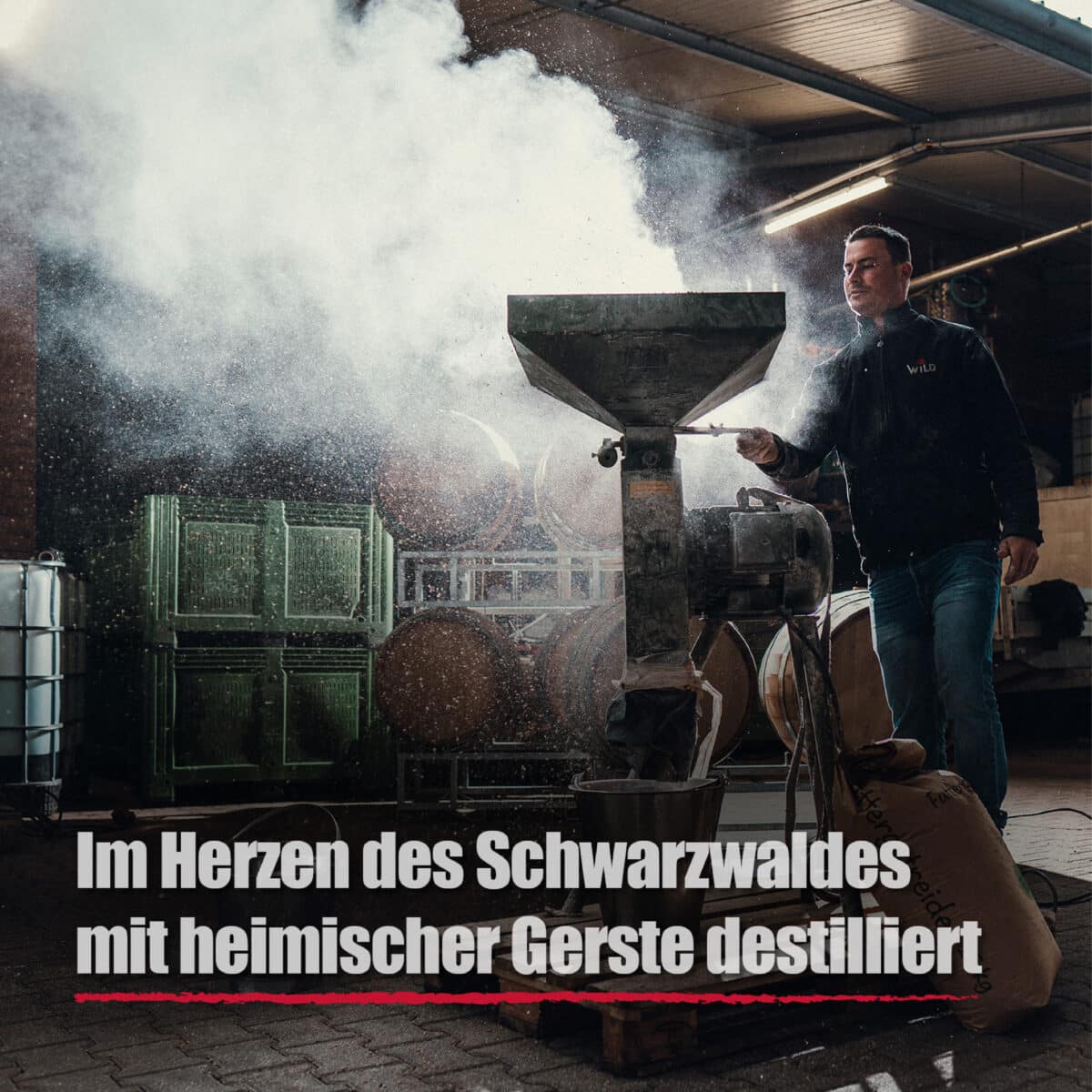 Ein Mann bedient eine staubende Getreidemühle in einer Destillerie, hinter ihm stapeln sich Fässer und Geräte. Das Bild ist mit deutschem Text versehen und wirbt für Blackforest Wild Vodka.