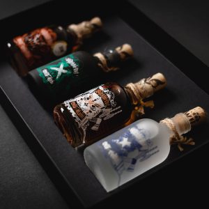 Die Blackforest Wild Spirits all in (0,2) mit Geschenketui besteht aus vier kleinen Glasflaschen mit illustrierten Etiketten und Korkstopfen, die jeweils mit einer andersfarbigen Spirituose gefüllt sind und in einer schwarzen Geschenkbox verpackt sind.