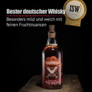 Eine Flasche Blackforest Wild Whisky Sherry Cask mit Korkverschluss steht auf Holz und ist mit einem rot-schwarzen Etikett, einer Medaille und einem deutschen Text versehen, der seinen milden, fruchtigen Geschmack hervorhebt.