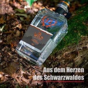 Eine Flasche Wilde Vogelbeere ruht auf moosbewachsenem Boden zwischen Blättern, im Vordergrund ist der deutsche Text "Aus dem Herzen des Schwarzwaldes" zu sehen.