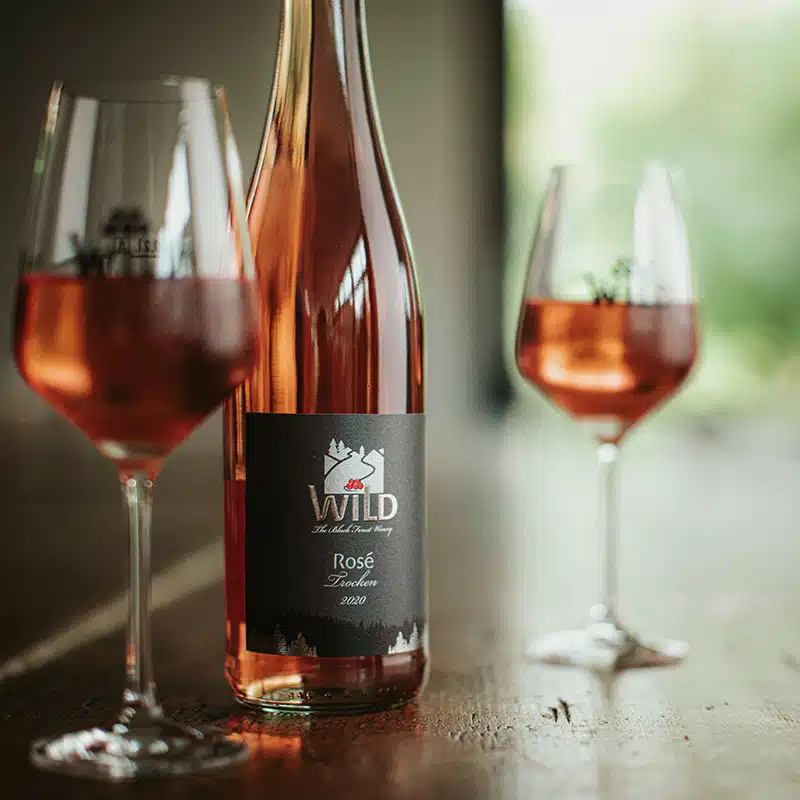 Eine Flasche Wild Rosé Wein mit zwei teilweise gefüllten Weingläsern auf einem Holztisch, mit unscharfem Hintergrund.