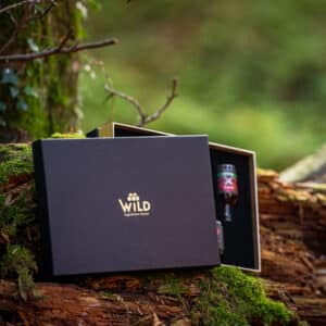 Eine Online-Verkostungsbox liegt geöffnet auf einem moosbewachsenen Baumstamm im Wald und enthüllt eine Flasche - perfekt für Ihr nächstes Verkostungsabenteuer.