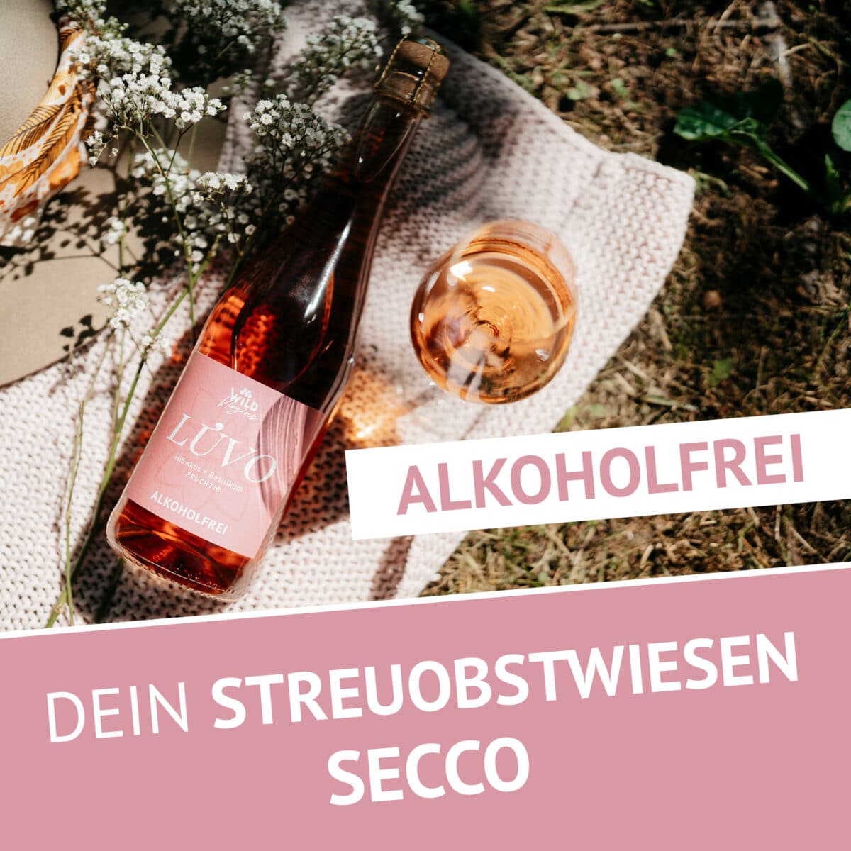 Eine Flasche und ein Glas LÚVO Hibiskus x Basilikum - Alkoholfrei rosé secco ruhen auf einer Decke mit Blumen; der Text lautet ALKOHOLFREI, Fine Spritz, und DEIN STREUOBSTWIESEN SECCO.