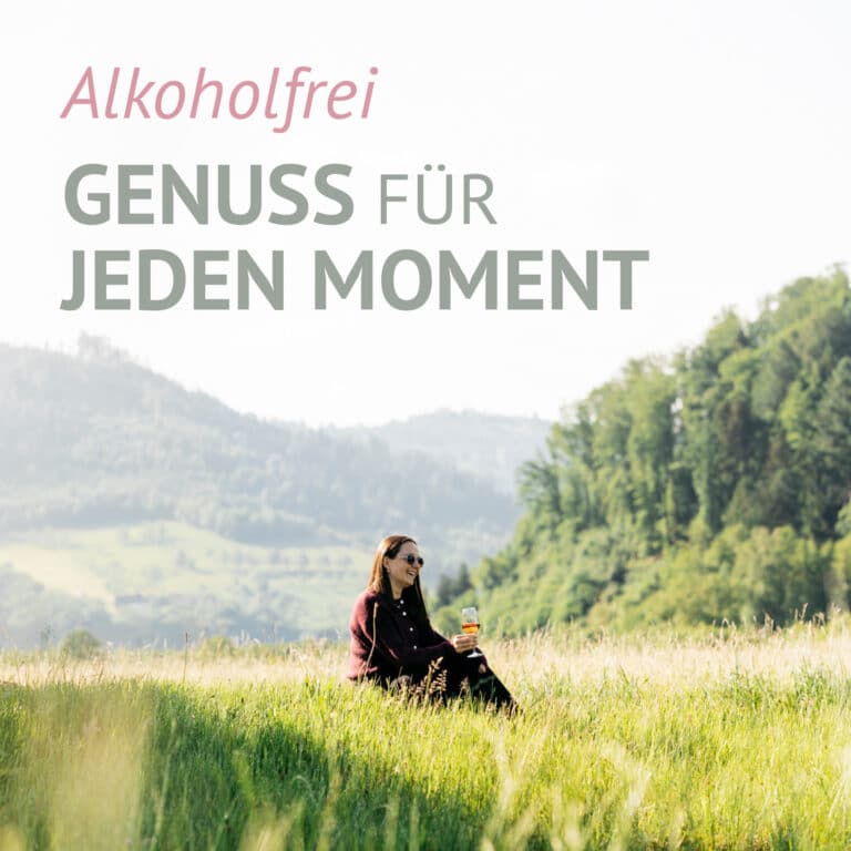 Eine Frau sitzt auf einer Wiese und hält einen LÚVO Hibiskus x Basilikum - Alkoholfrei in der Hand. Im Hintergrund sind Hügel und Bäume zu sehen. Der Text auf Deutsch lautet "Alkoholfrei Genuss für jeden Moment".