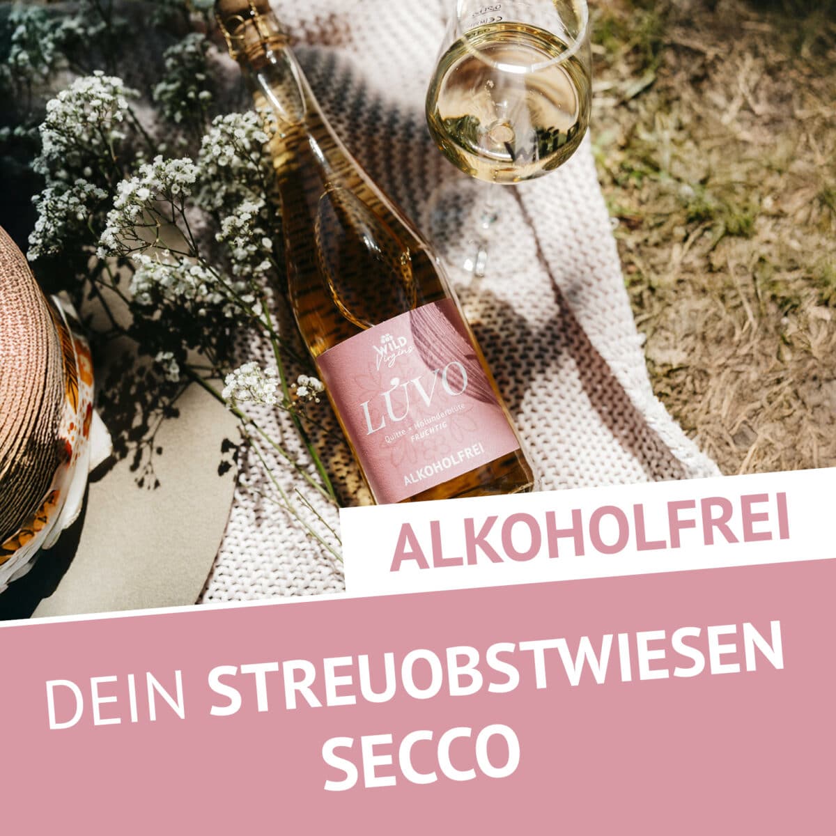 Eine Flasche LÚVO Quitte x Holunderblüte - Alkoholfrei ruht auf einer Decke neben einem Weinglas und Blumen. Der Text lautet: ALKOHOLFREI DEIN STREUOBSTWIESEN SECCO.